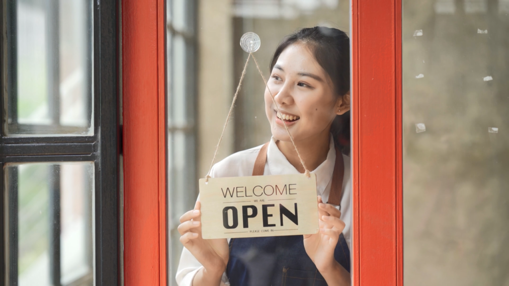 Photo of business owner displaying open sign at their business entrance.